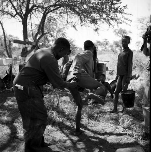 Man leaping away after receiving a shot from the expedition doctor, with people standing in the background