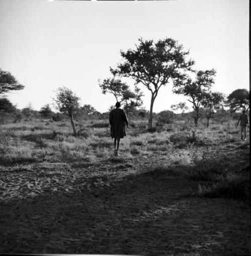 Man wearing a Western coat and a hat walking, distant view from behind