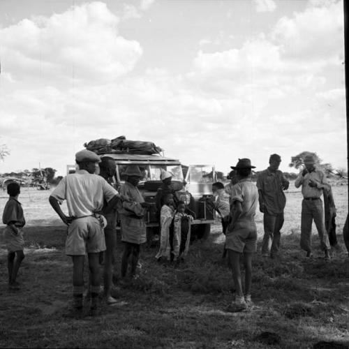 Group of men standing with John Marshall and two other expedition members next to the expedition Jeep