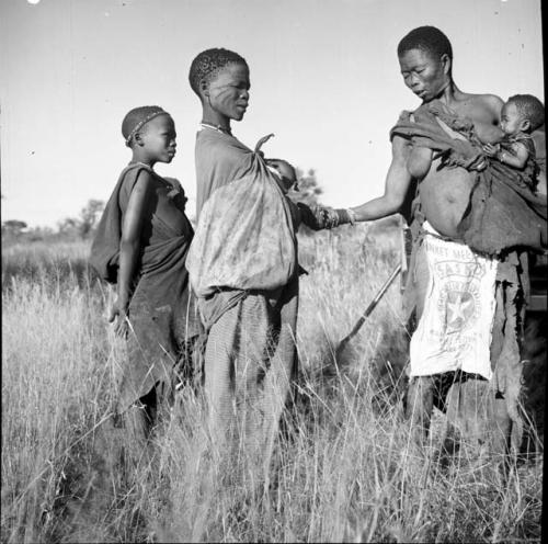 !Ungka wearing a cloth food bag as a modesty apron, carrying a baby, standing with two other women and a child