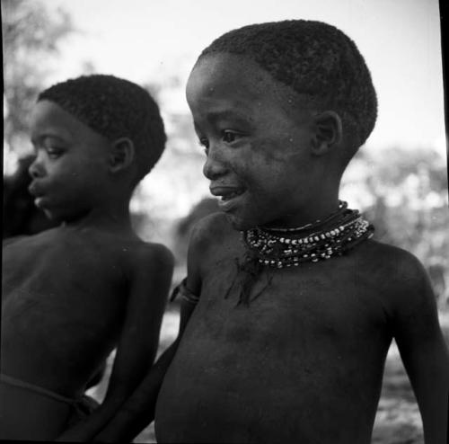 Two children sitting, one wearing necklaces