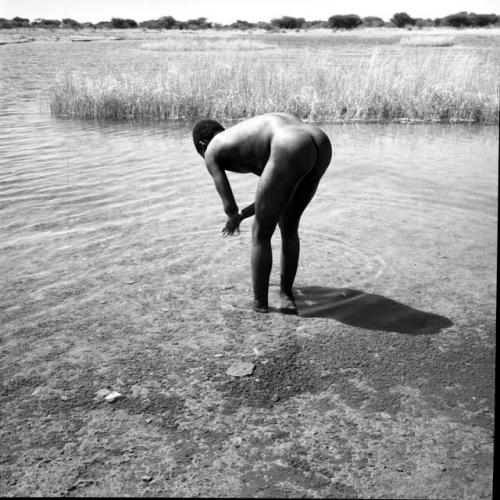 Man standing in the water in a pan, leaning over, washing his hands