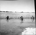 Three men sitting in the water in a pan, bathing