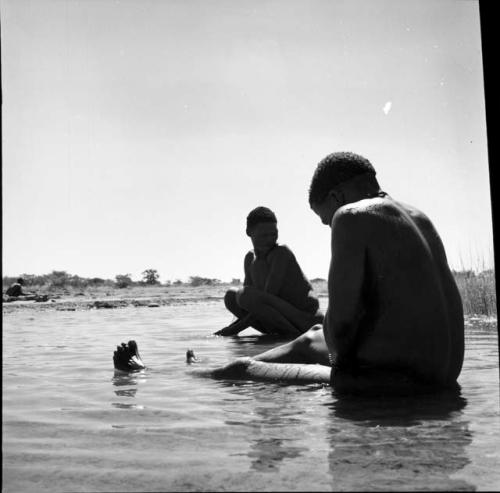 Two men sitting in the water in a pan, bathing