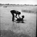 Man leaning over, scrubbing the back of another man in the water in a pan