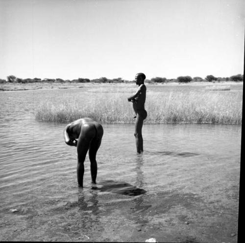 Two men standing in the water in a pan, one leaning over