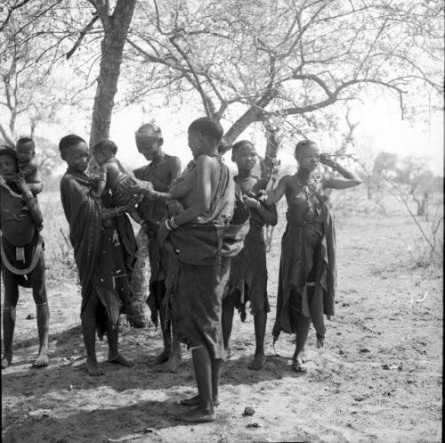 Group of women standing underneath trees, with one woman handing a crying baby to another in the back