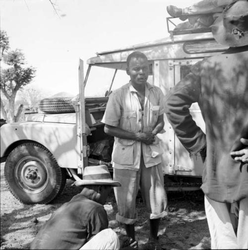 Men standing and sitting next to an expedition member standing in front of the Land Rover