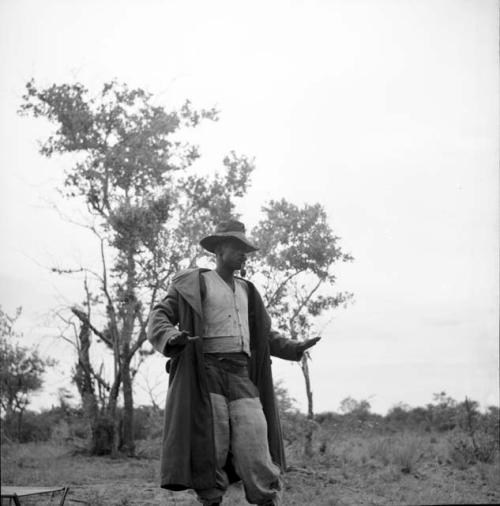 Man from Kubi standing, smoking a pipe, with his axe and an expedition chair on the ground next to him