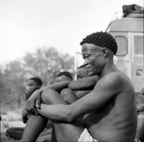 /Ti!kay sitting with three other men in front of the expedition Land Rover