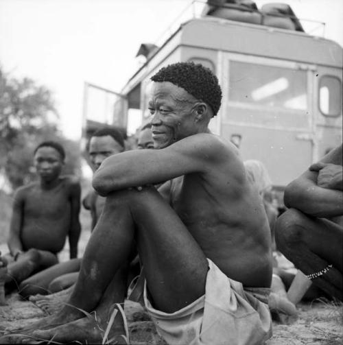 /Ti!kay sitting with three other men in front of the expedition Land Rover