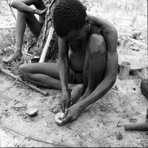 Bojo extracting poison from a grub in a dish made from a wildebeeste knee bone