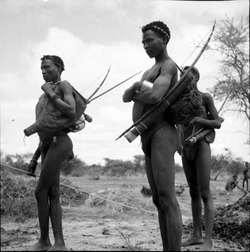 Three men standing, carrying hunting equipment, including a spring hare pole