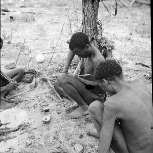 Bojo making an arrow from a rough stick, sitting with another man