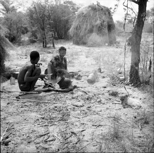 Man and woman cooking at a fire, with a skerm in the background