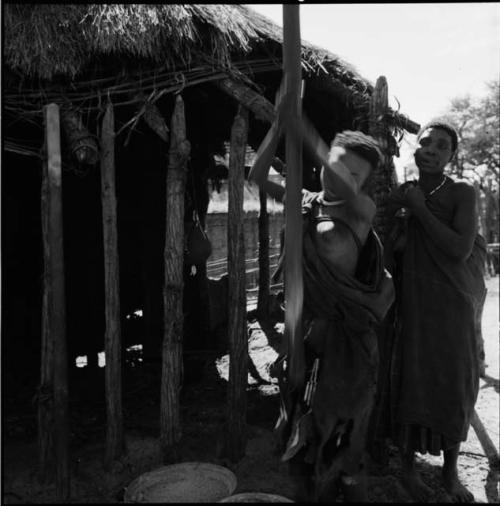 Woman pounding corn, with another woman standing behind her