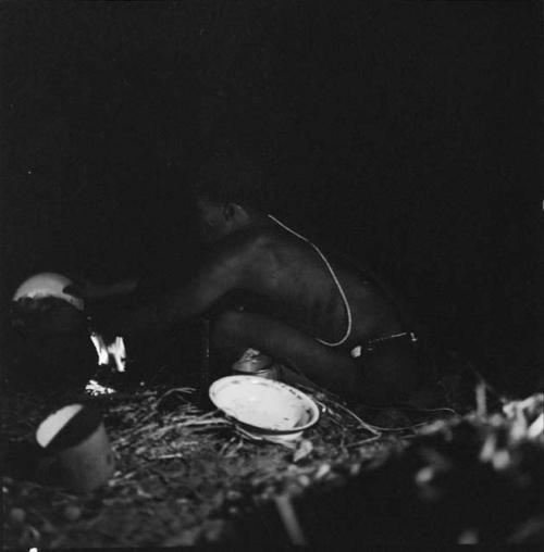 Man cleaning a pot, with other utensils lying on the ground next to him