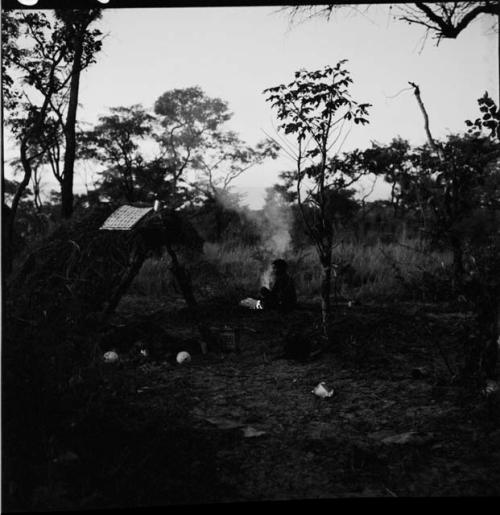 Man sitting next to a fire near a shelter skerm, with two ostrich egg shells on the ground beside it