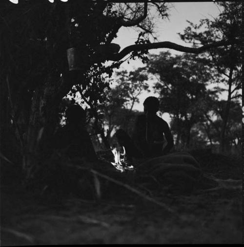 Man sitting with another person next to a fire near a shelter skerm