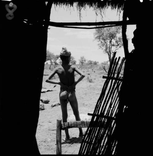 Boy wearing a hat, standing, view from behind, from within a skerm