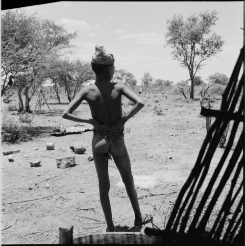 Boy wearing a hat, standing outside a skerm, view from behind