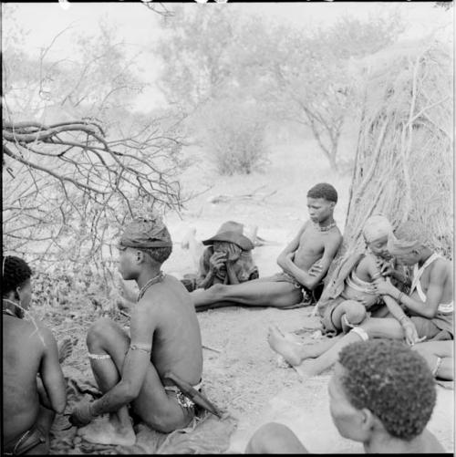 Man fixing a woman's arm ornaments, sitting with a group of people