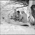 Man adjusting one of the pegs on a //guashi, sitting with a group of people