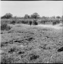 People stand in and next to a pan with water in it, distant view