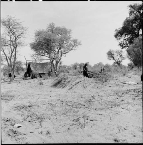 Man standing next to the foundation of a skerm, with people standing near an expedition tent in the background