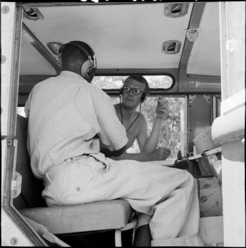 Nicholas England wearing earphones, sitting with another staff member in an expedition truck, talking