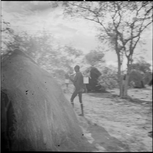 Man walking next to a skerm, carrying an enamel bucket on his carrying stick