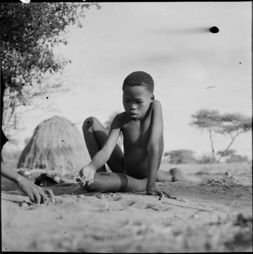 Boy playing /Ui (the counting game) in the sand with another boy whose hand is visible