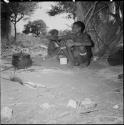 Two men sitting next to a skerm, with a large iron pot on a fire near them