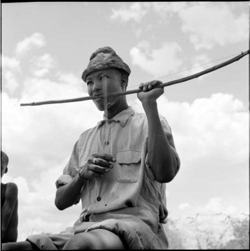 /Gaishay wearing Western clothing, sitting on an oil can, playing a one-stringed bow