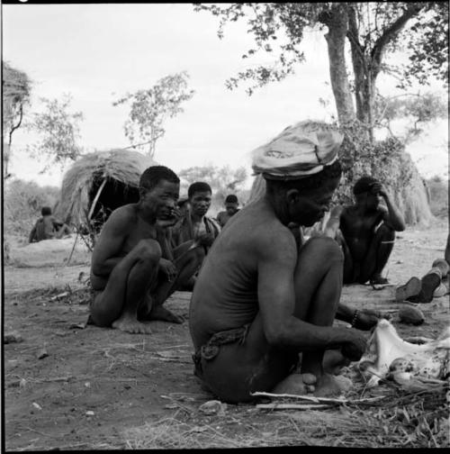 ≠Toma skinning an animal, sitting with /Ti!kay and other men, with skerms in the background