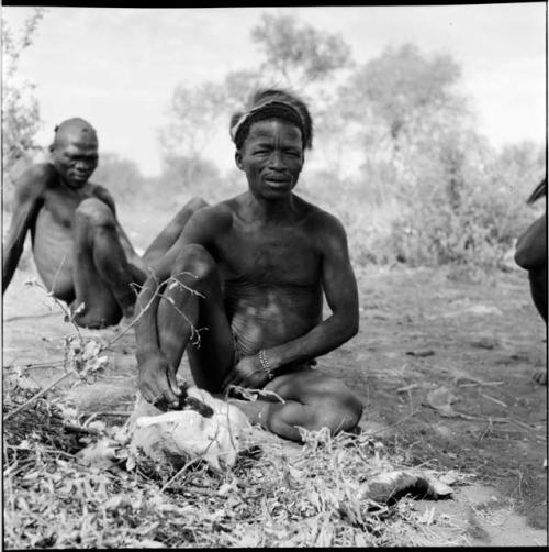 ≠Toma skinning an animal, with another man sitting behind him