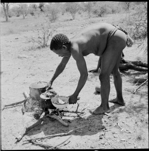 Man standing, leaning over to transfer food out of cooking pot into his enamel dish