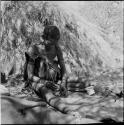 Woman sitting next to a skerm, drilling holes in ostrich eggshell beads