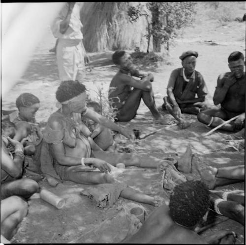 !U sitting with a group of people, holding a piece of string for ostrich eggshell beads