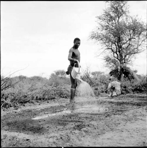 /Ti!kay watering plowed land with a watering can