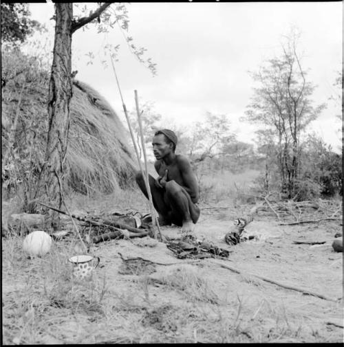 Man squatting near a skerm, with hunting equipment on the ground next to him