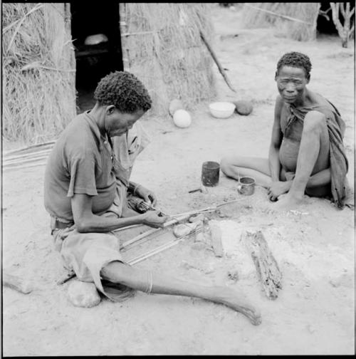 Man taking arrows out of a quiver, sitting with another man in front of a skerm