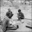 "Gao Medicine" sitting with a man holding an assegai blade and another man, with arrows and Sansiveria leaves on the ground next to them