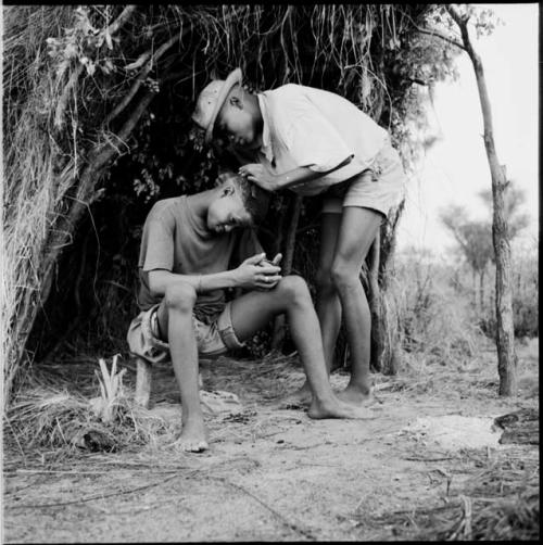 Tsamgao examining !Naishi's hair in the opening of a skerm