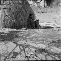 Man sitting, leaning against a skerm, a hide pegged to the ground near him, a dried hide on the other side of him