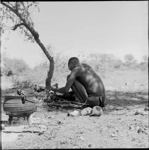 Man preparing meat for cooking, view from behind, with a pot on the ground near him
