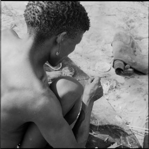 Man wearing a safety pin in his ear, applying poison to an arrow shaft