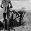 Gau (husband of Be and Khuan//a) working on the neck of a dead wildebeest, with another man standing, watching him