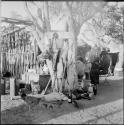 Men sitting and standing in the expedition camp, view from behind, with a hen and chicks on the ground near them