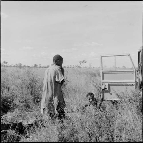 Man standing, with another sitting next to the expedition Jeep